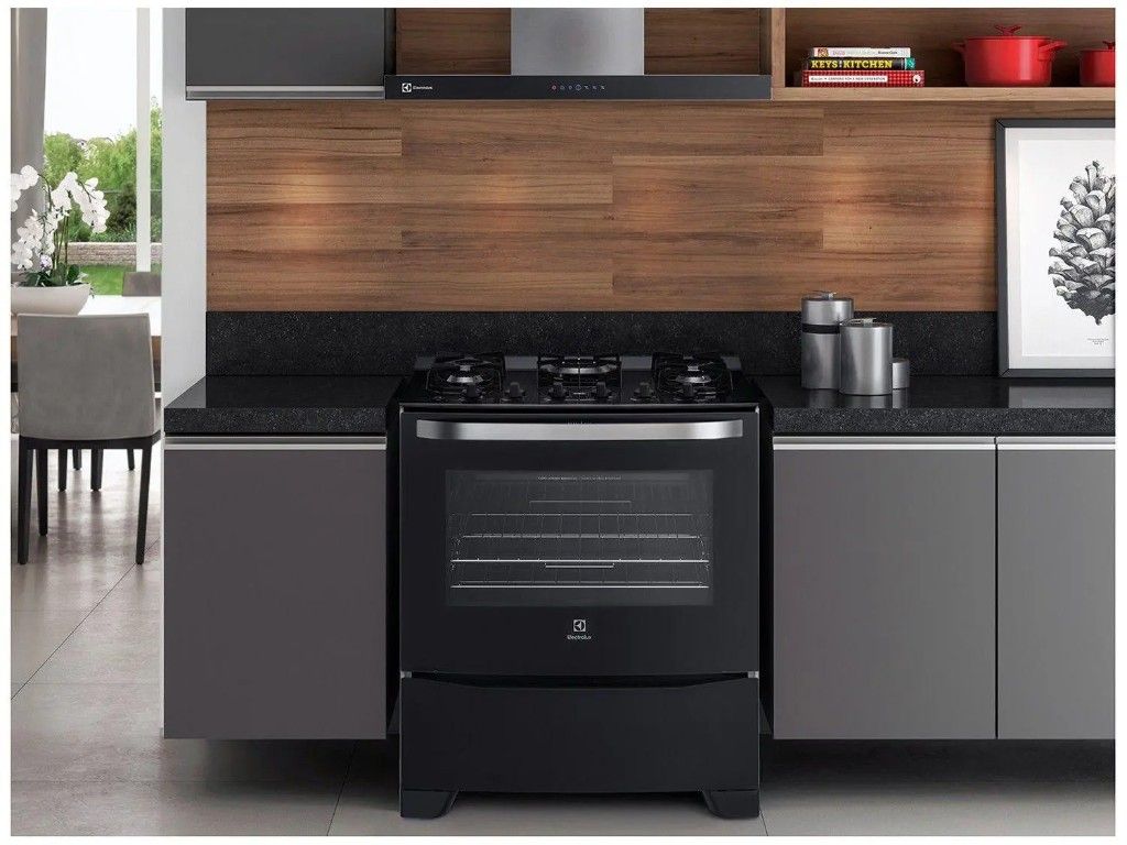 Cozinha moderna com fogão Electrolux de cinco bocas preto com porta de vidro, integrado entre armários escuros e bancada de granito.